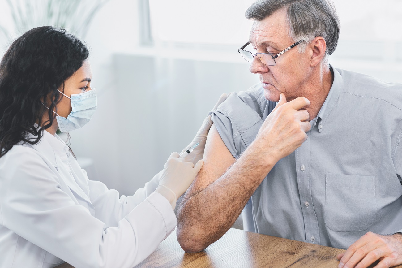 An elderly man is receiving his flu vaccination from his doctor